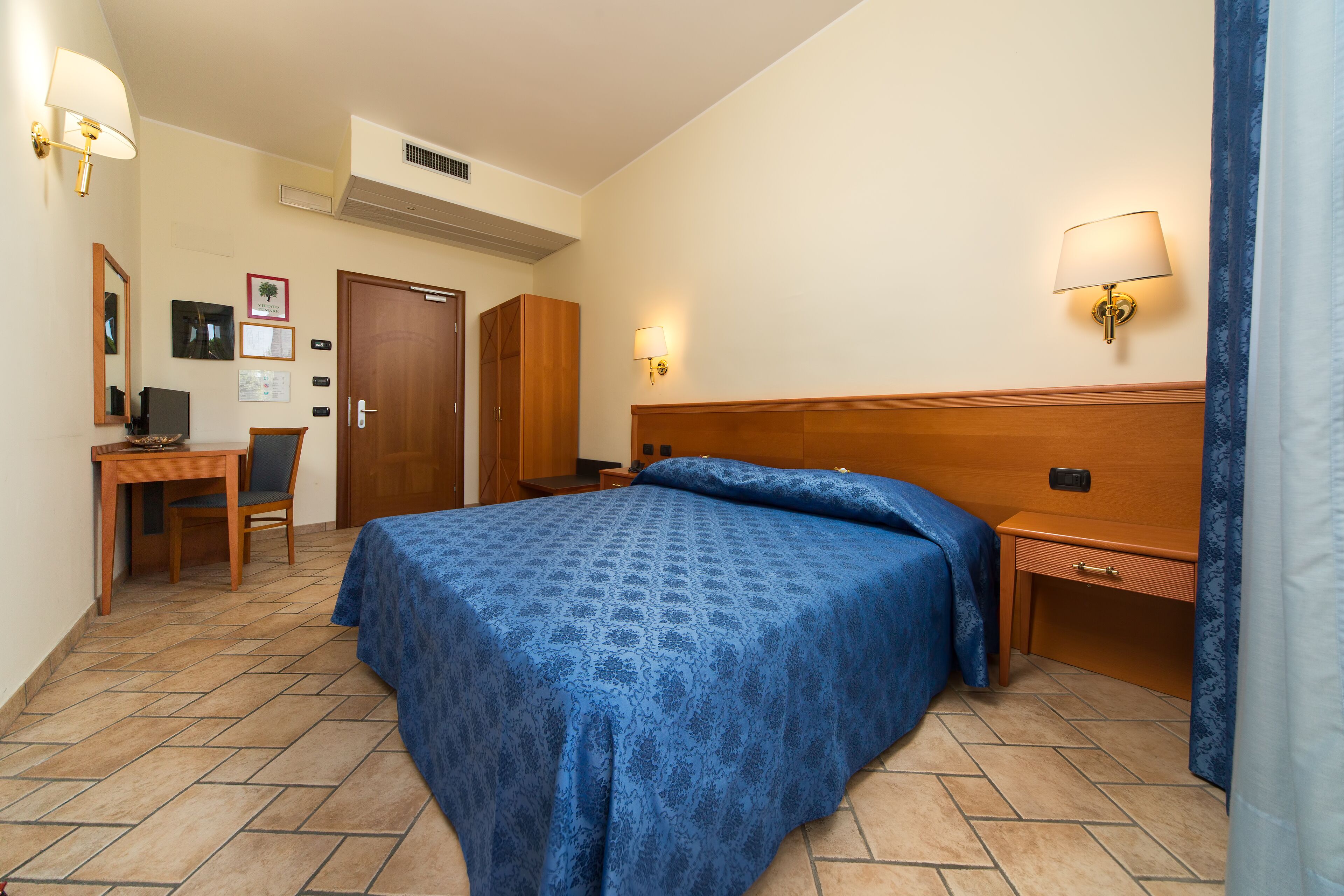 A hotel room with a bed, a desk, a chair, a wardrobe, and a nightstand.
