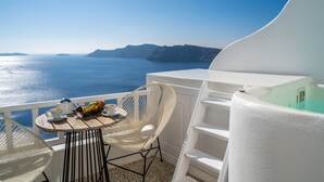A balcony with a table set for breakfast, overlooking the sea and a white building. - Delfini Villas (Santorini)