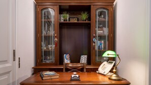 A wooden desk with a telephone, a lamp, and a chair. Behind the desk is a wooden cabinet with glass doors containing books and decorative items. - Delfini Villas (Santorini)