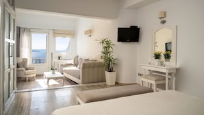 A hotel room with a large window, a bed, a sofa, a desk, and a TV. - Delfini Villas (Santorini)