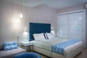 Um quarto moderno com uma cama grande, mesa de cabeceira, uma cadeira e um guarda-roupa.