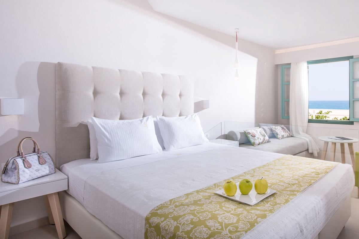 Een hotelkamer met een groot bed, een nachtkastje met een lamp, een stoel en uitzicht op zee.