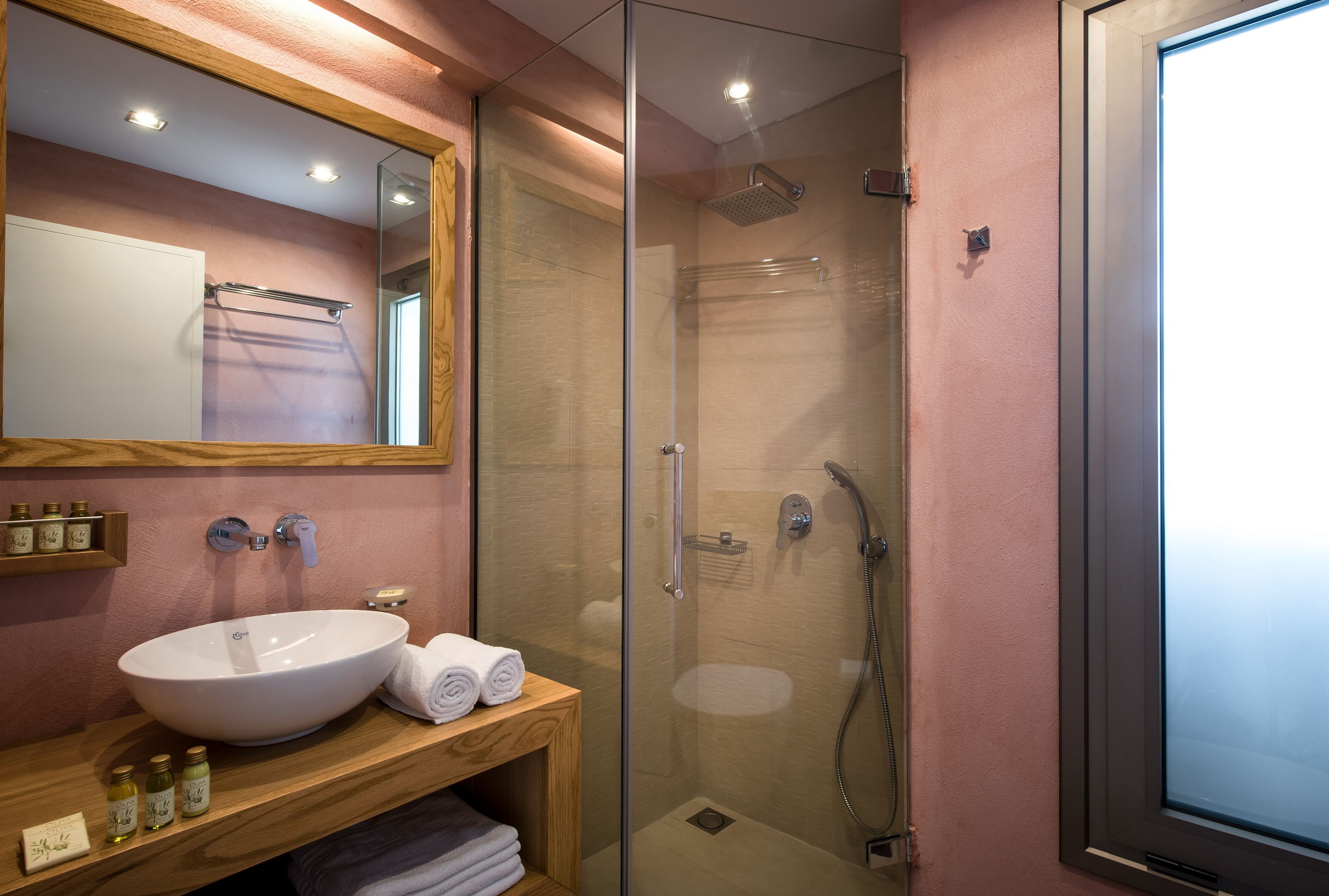 A modern bathroom with a large white sink, a glass-enclosed shower, and a wooden vanity with toiletries.