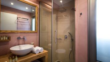 A modern bathroom with a large white sink, a glass-enclosed shower, and a wooden vanity with toiletries.