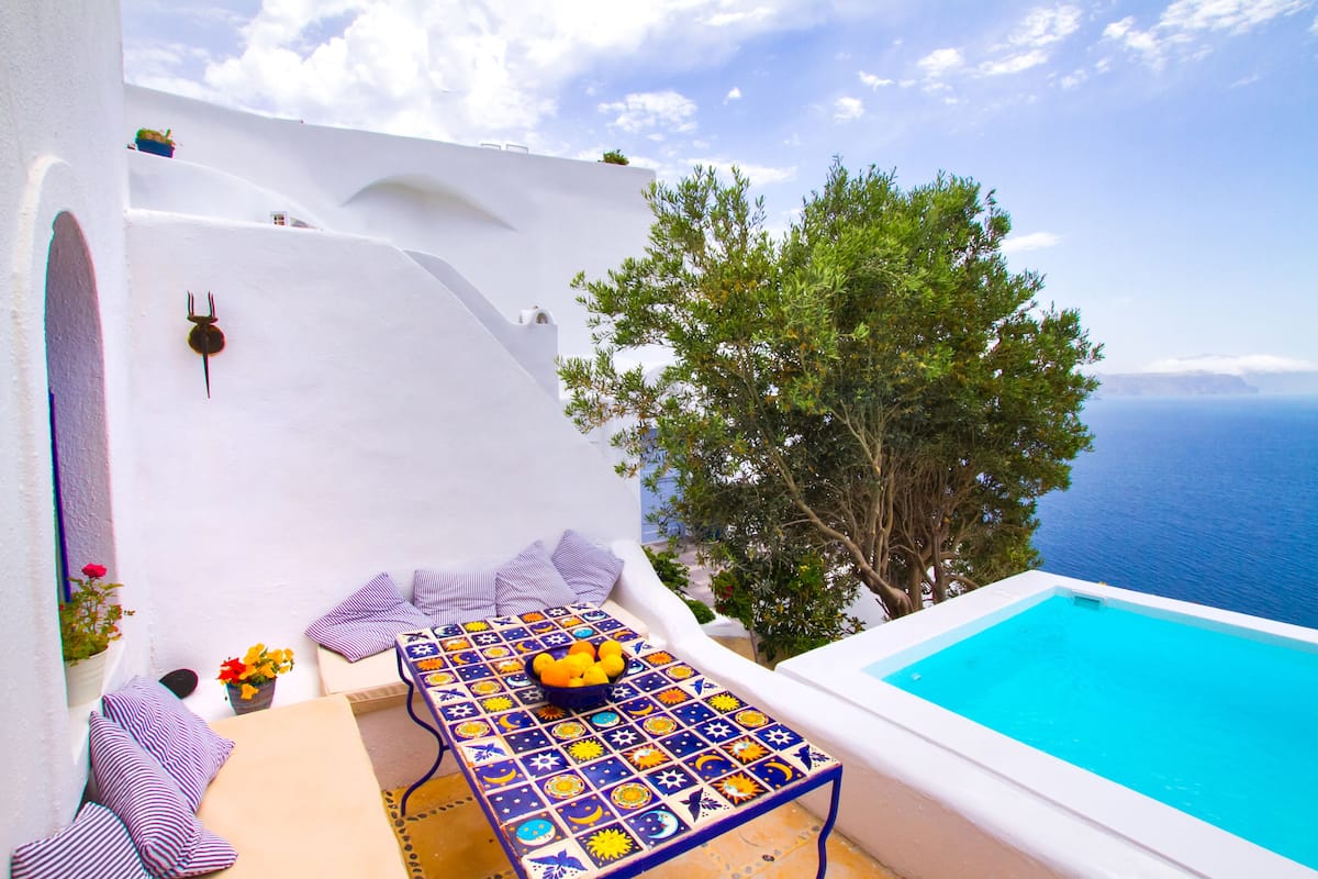 Ein Zimmer mit weißen Wänden, einem Pool, einem Tisch mit Obstschale und Blick aufs Meer.