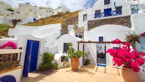 Un edifici blanc amb portes i finestres blaves, envoltat de plantes i flors en testos.