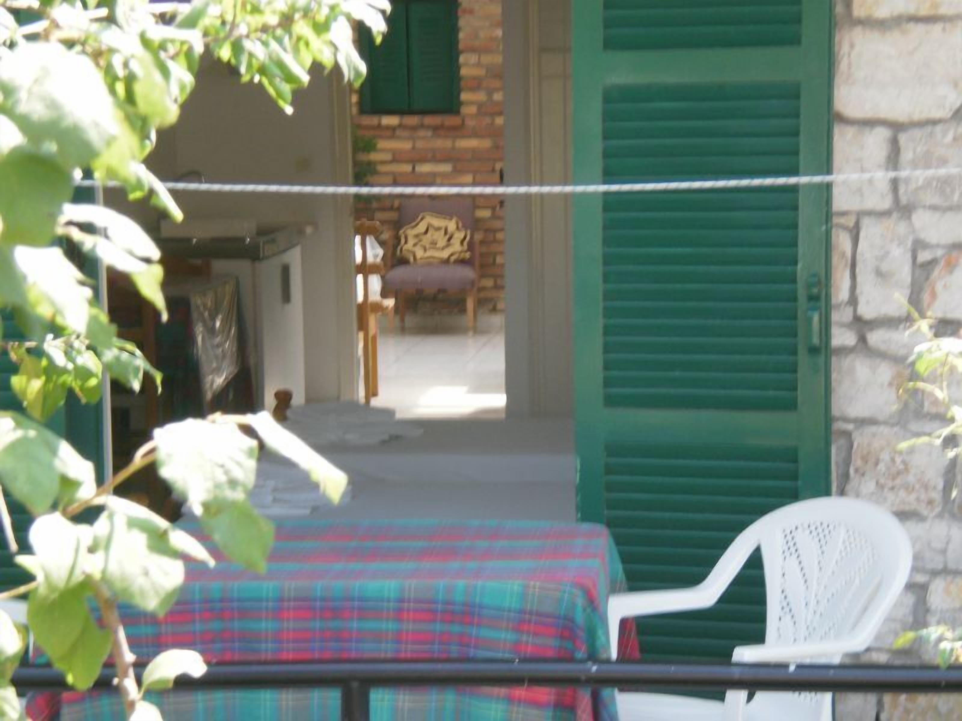 A room with a plaid tablecloth, a white plastic chair, and a green shuttered door.
