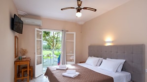 A bedroom with a bed, a ceiling fan, a TV, and a window with a view of greenery.