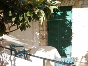 Un patio con mesa y sillas, una puerta con persiana verde y una pared de piedra.