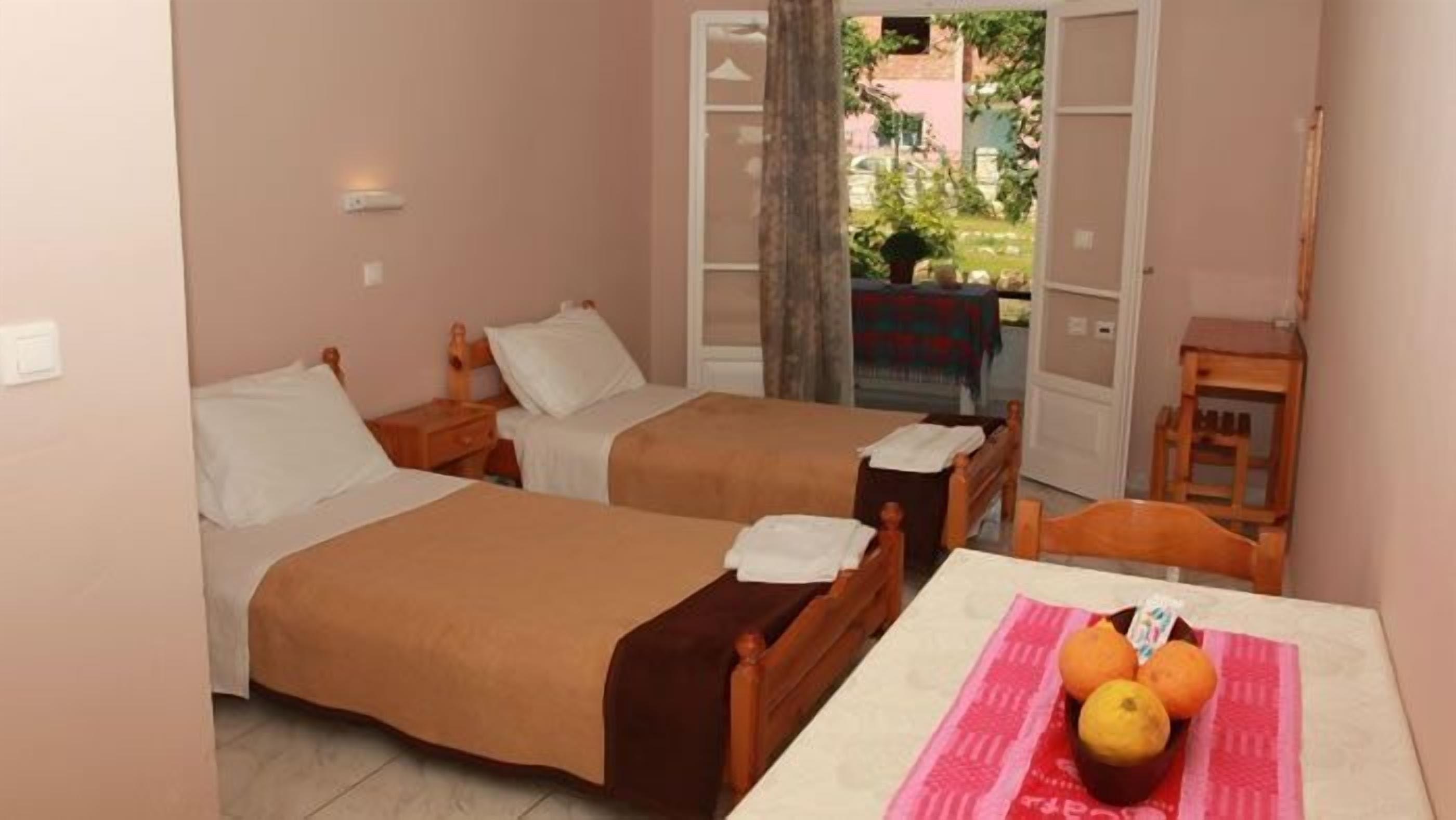A hotel room with two beds, a small table with fruit, and a view of the outside.