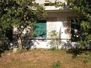 Un edificio con fachada de piedra, contraventanas verdes y un pequeño jardín con césped y arbustos.