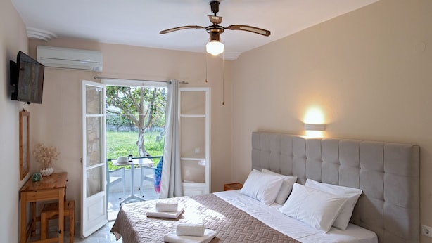 A bedroom with a bed, a ceiling fan, a TV, and a balcony with a view of greenery.