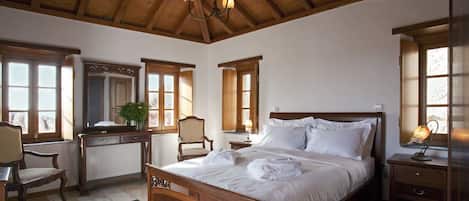 A bedroom with a wooden ceiling, a large bed, a desk, and a chair.