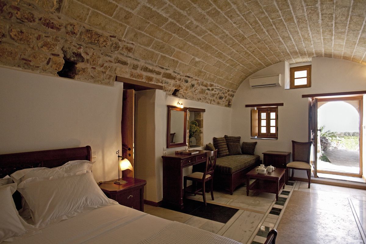 A bedroom with a bed, a desk, a chair, a sofa, and a window.
