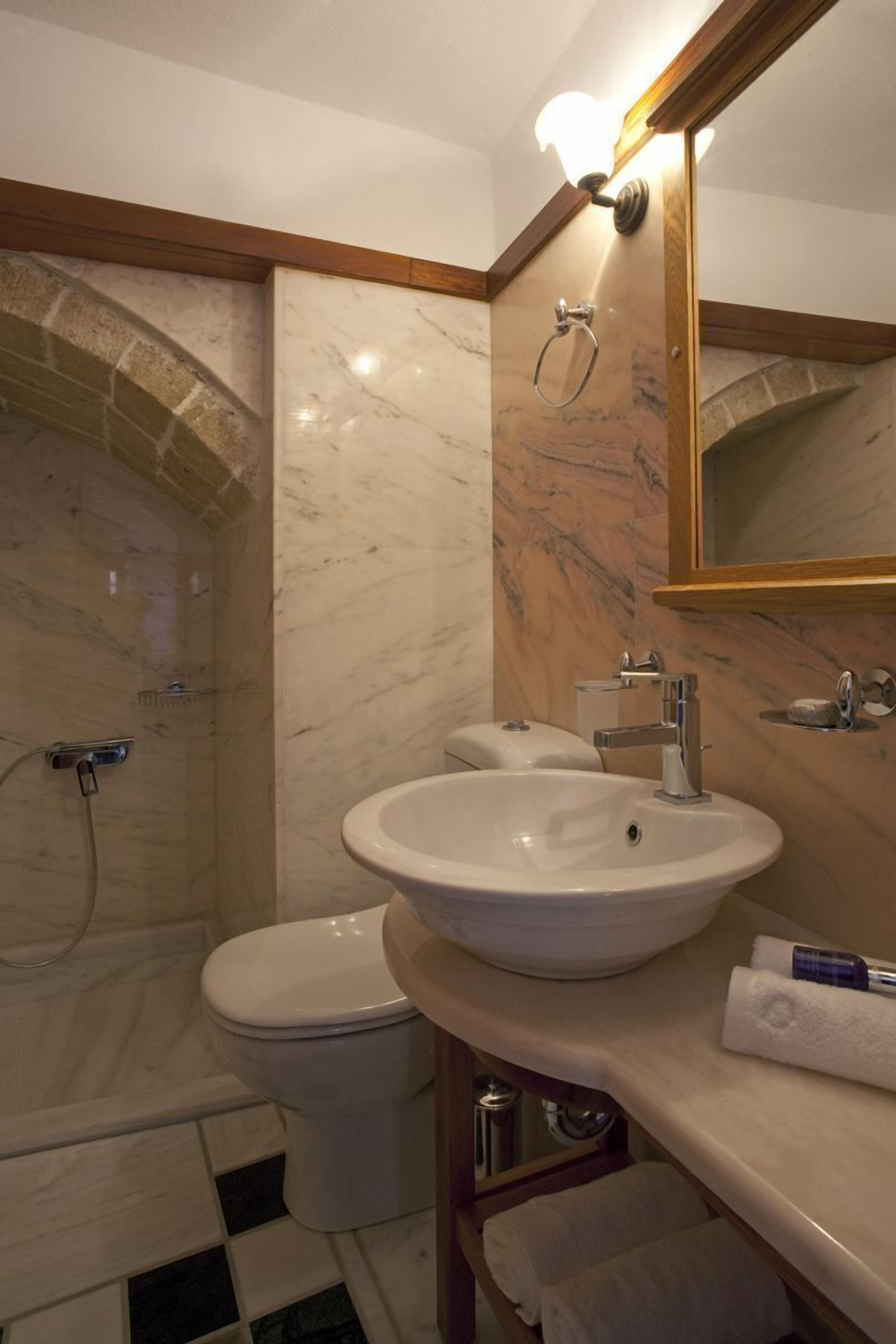 Et badeværelse med bruser, toilet, håndvask og spejl.