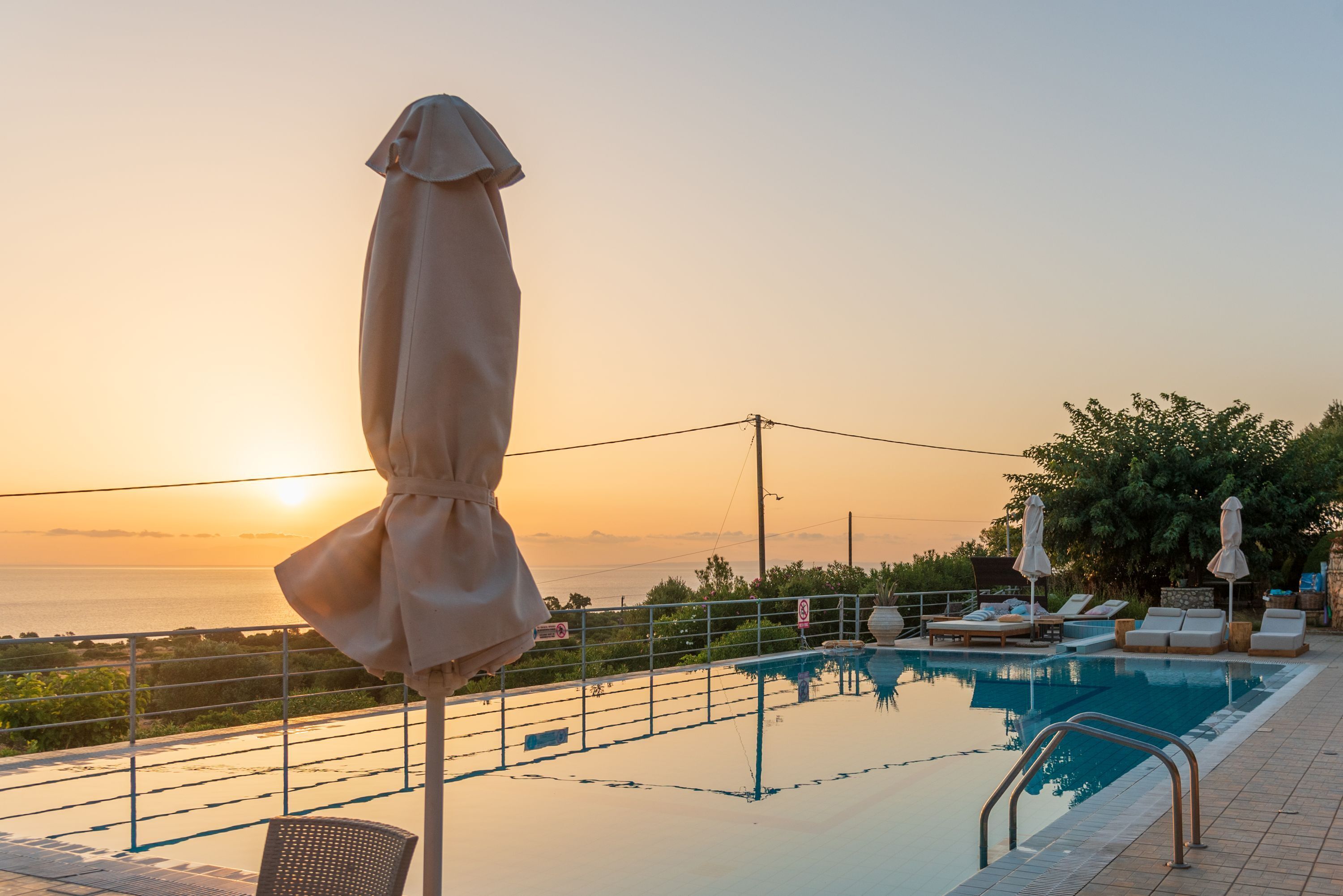 A poolside area with lounge chairs and umbrellas, overlooking a body of water during sunset.