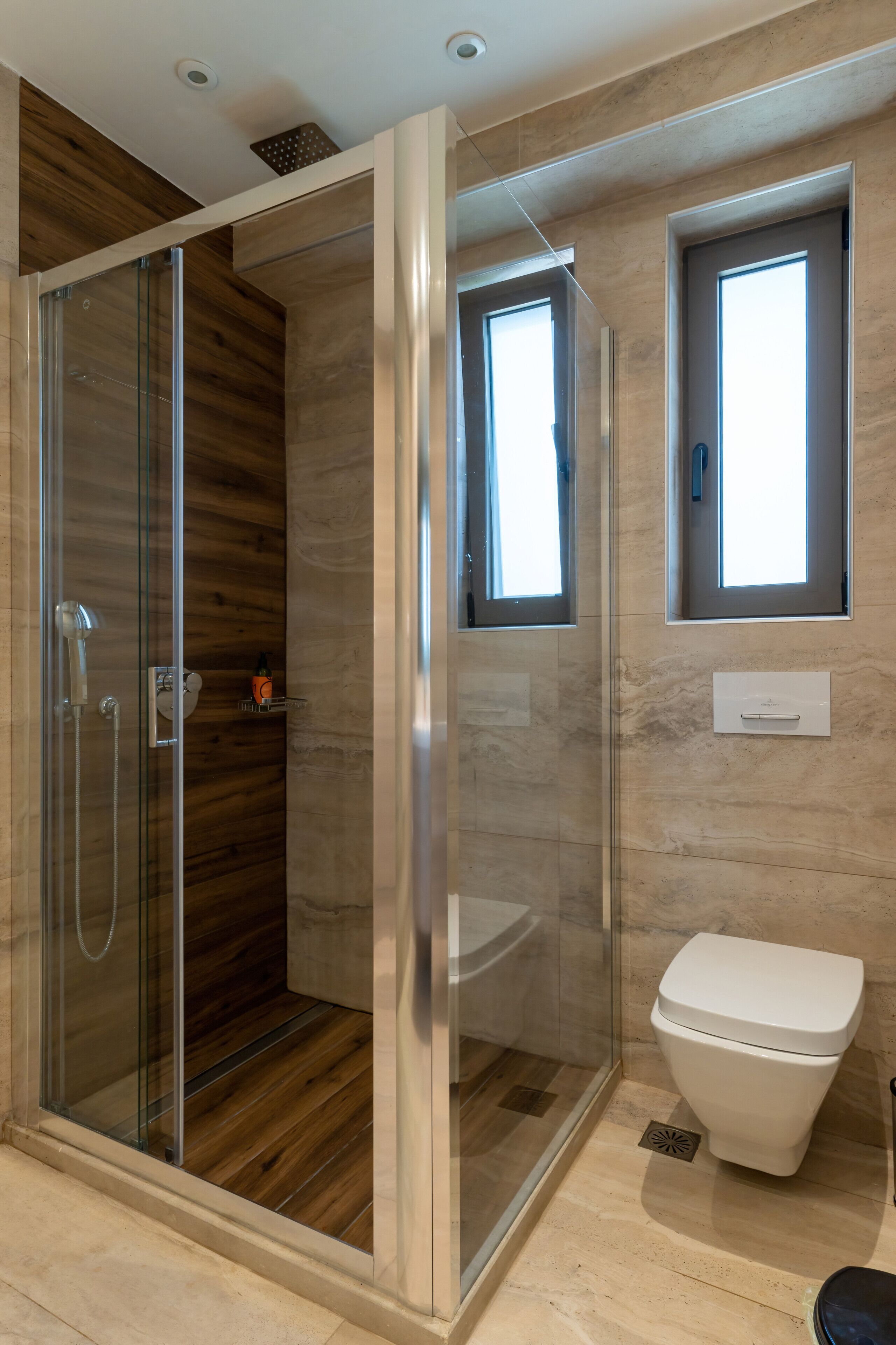 Een moderne badkamer met een douchecabine van glas, een toilet en een raam.