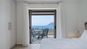 Un dormitorio con una cama grande, un balcón con mesa y sillas, y vistas al mar y a la montaña.