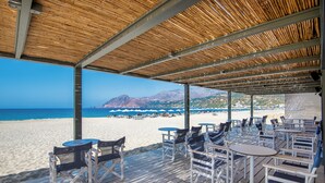 Un patio frente a la playa con mesas y sillas, con vistas a una playa de arena y al océano.