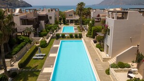 Un moderno resort con piscina central, rodeado de jardines cuidados y palmeras.