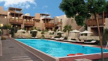 Una piscina con sillones de descanso y sombrillas, rodeada de muros de piedra y un cielo azul despejado.