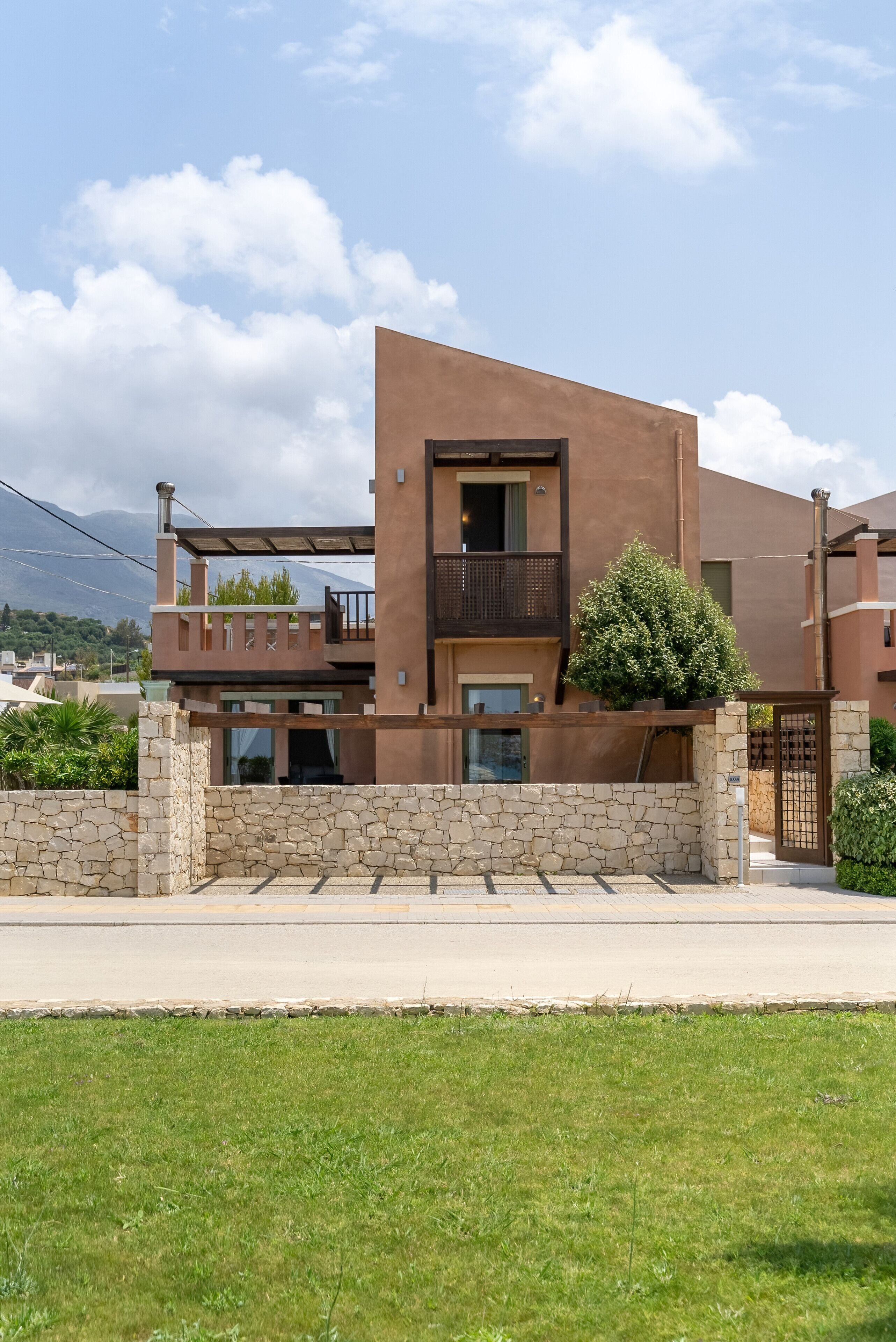 A modern two-story house with a stone facade, a balcony, and a small tree in the front yard.