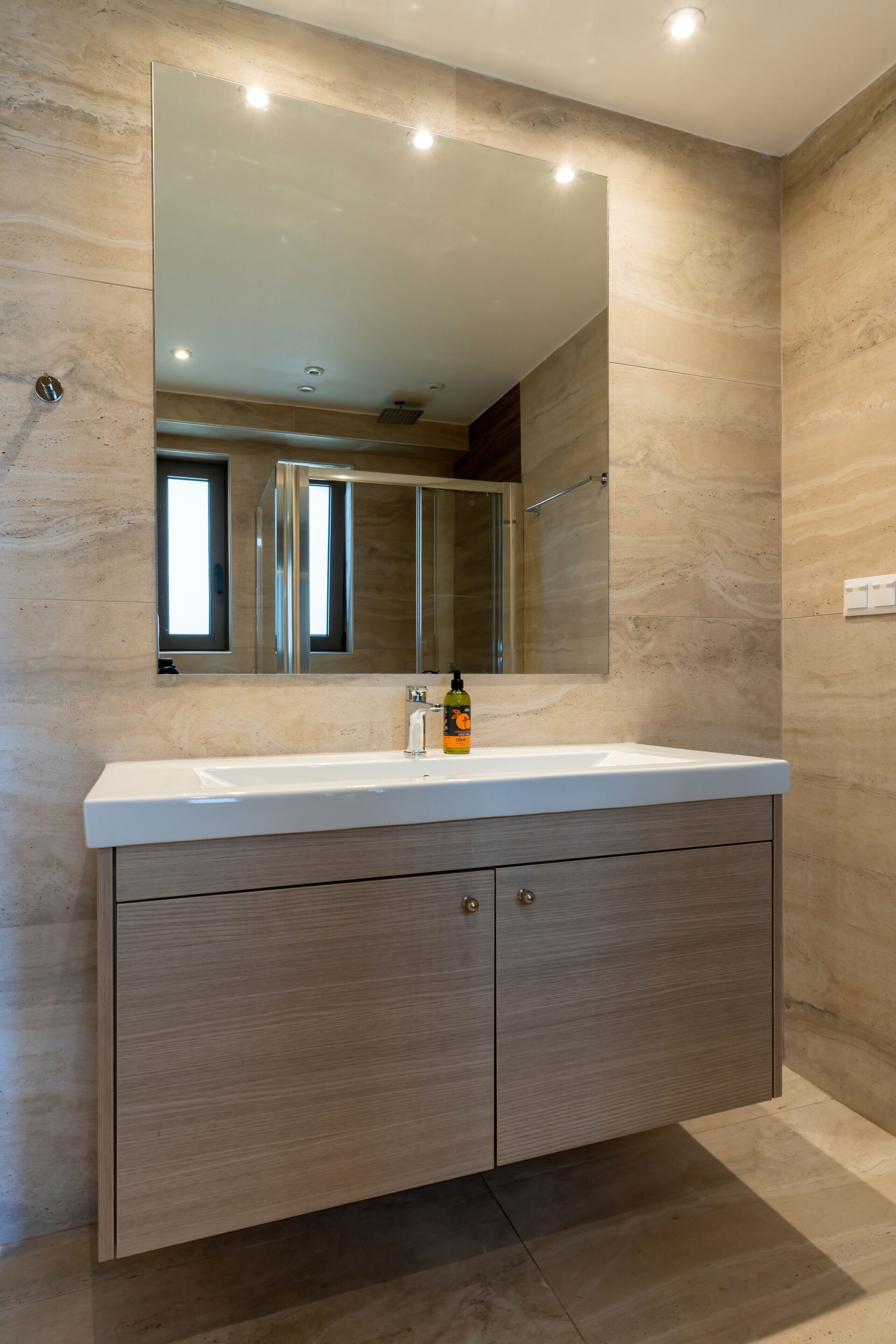 A modern bathroom with a large mirror, a white sink, and wooden cabinetry.