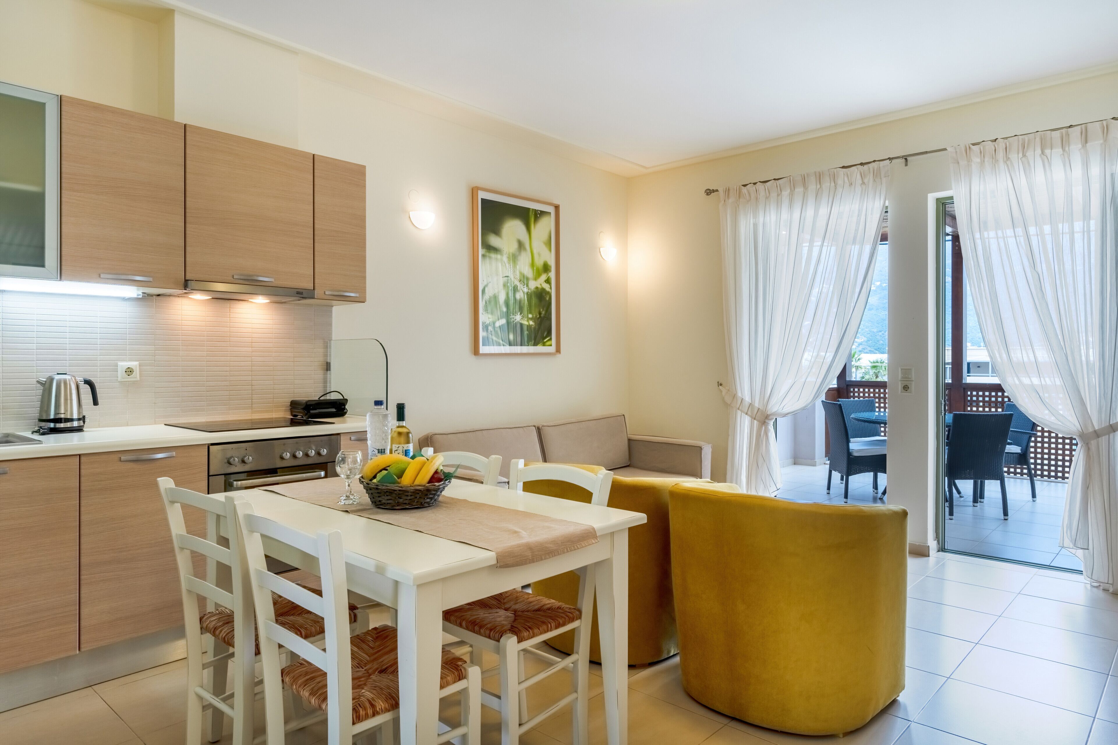 A modern kitchen with white cabinets, a dining area with a yellow chair, and a view of an outdoor patio.