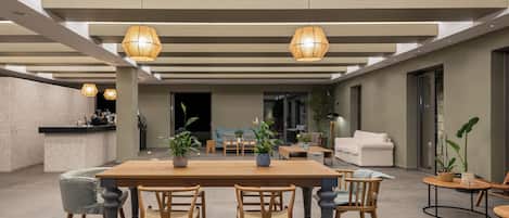A spacious living area with a wooden dining table, chairs, and hanging pendant lights. There is a sofa and a coffee table in the background.