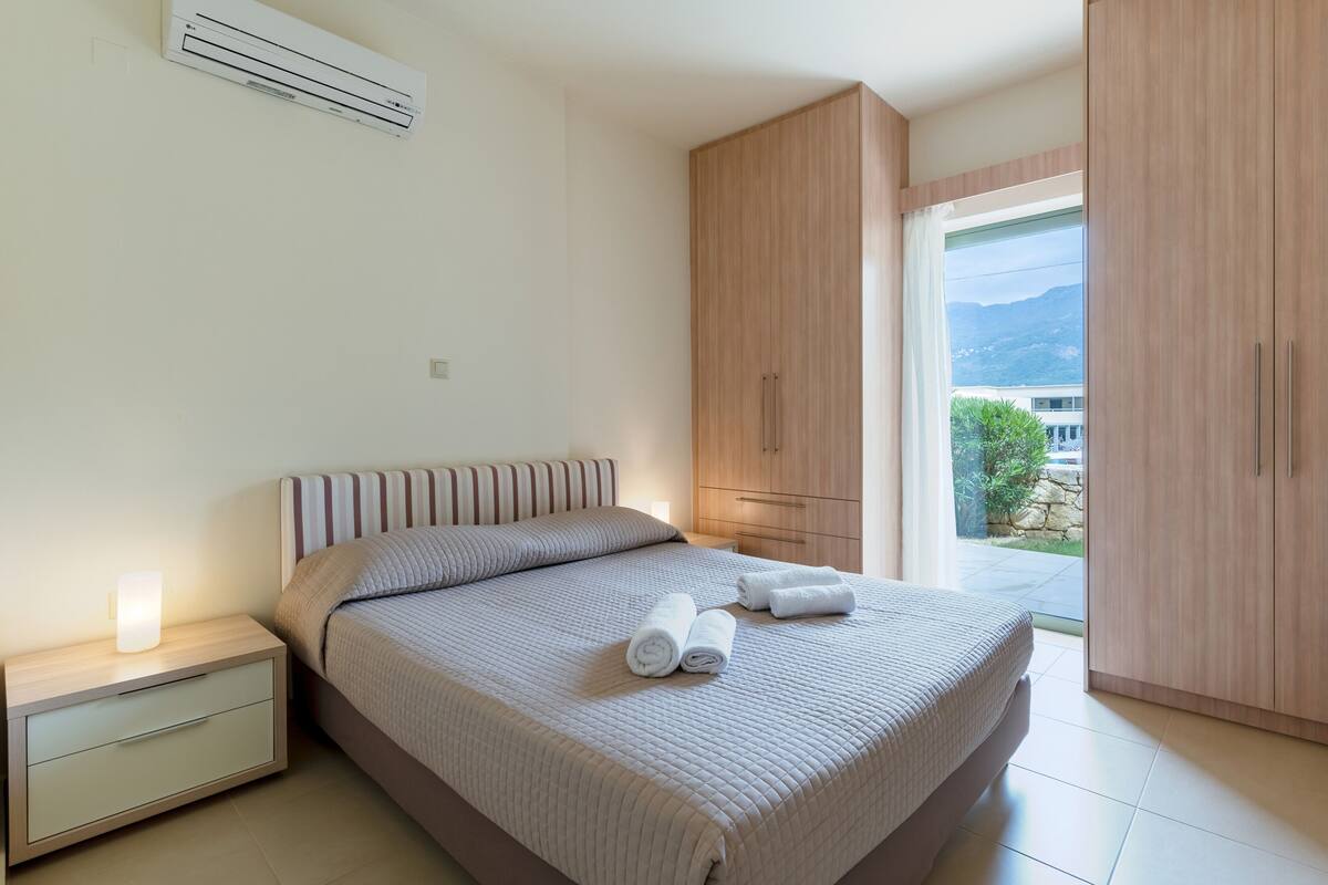 Un dormitorio moderno con una cama grande, una mesita de noche, un armario de madera y vistas al exterior.