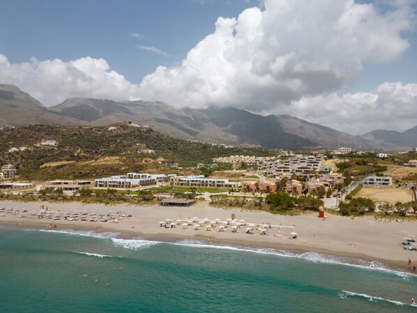 Un resort costero con villas frente a la playa, una playa de arena y montañas al fondo.
