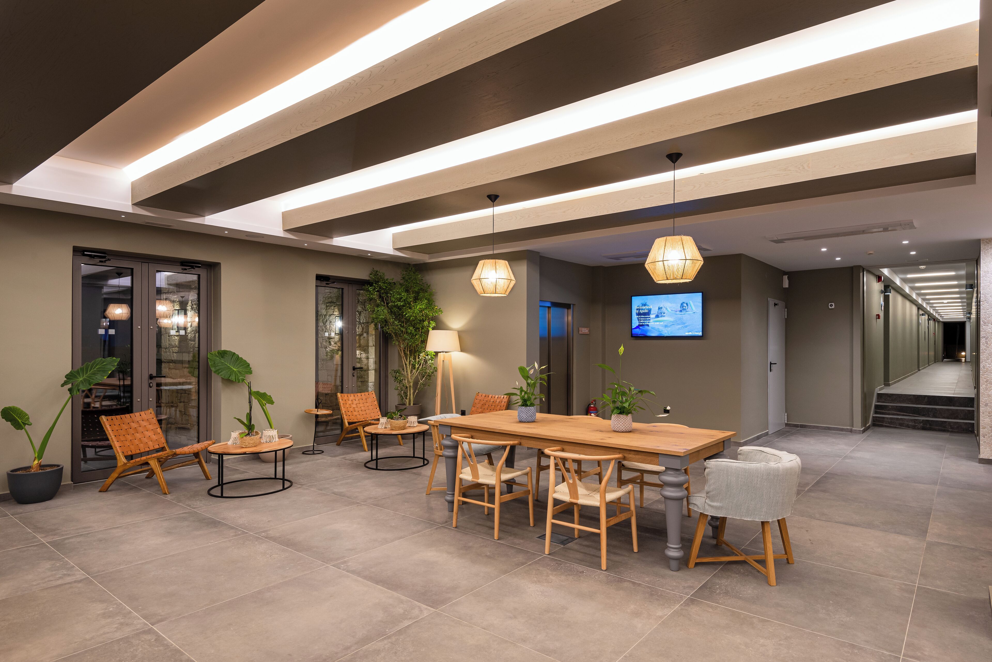 Un moderno vestíbulo de hotel con un mostrador de recepción de madera, asientos cómodos, plantas en macetas y un televisor de pantalla plana en la pared.