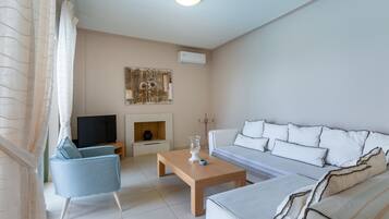 A living room with a sofa, armchair, coffee table, TV, fireplace, and artwork on the wall.