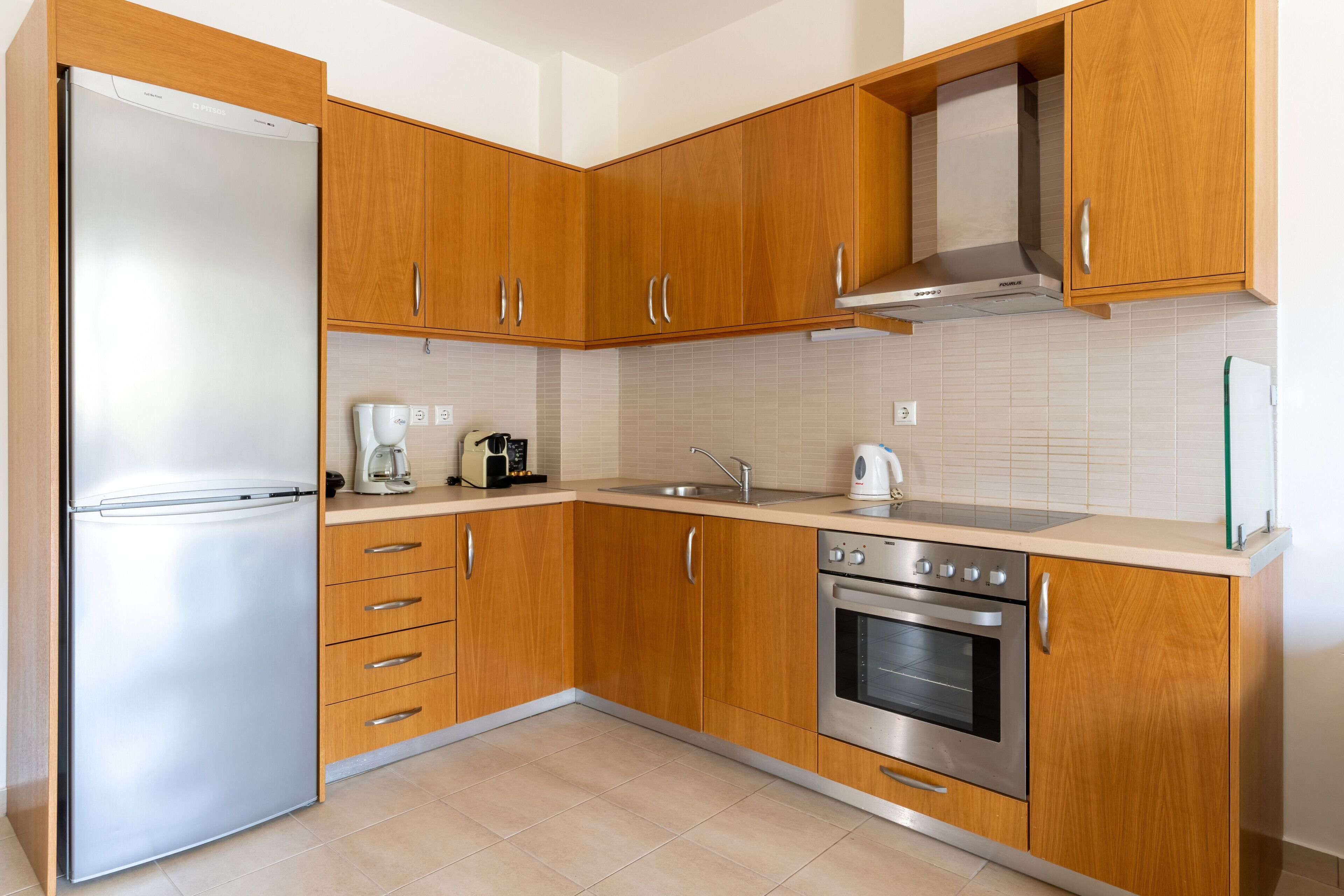 Una cocina moderna con armarios de madera, un refrigerador de acero inoxidable, un horno empotrado y una cafetera.