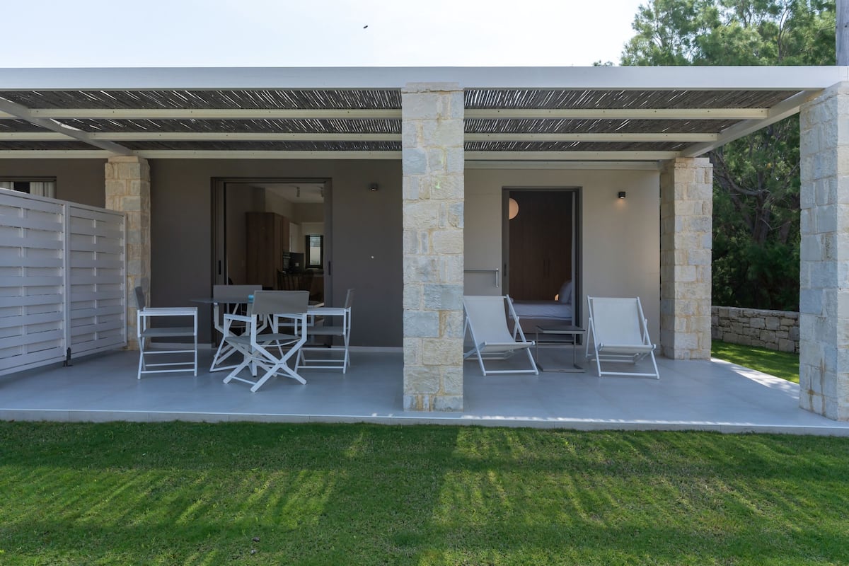 Un patio al aire libre cubierto con una columna de piedra, una mesa con sillas y sillones de descanso.