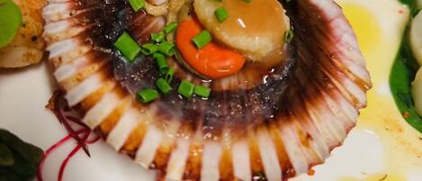 A dish with a scallop shell, garnished with green onions and a carrot.