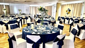 A banquet hall with round tables set for dining, white chairs with navy sashes, and floral centerpieces.