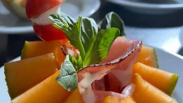 A dish with melon slices, a cherry tomato, basil, and a skewer.