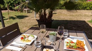 An outdoor dining table with two plates of food, glasses of wine, and a potted plant. - The Originals City, Hôtel Le Louisiane (Andelnans)