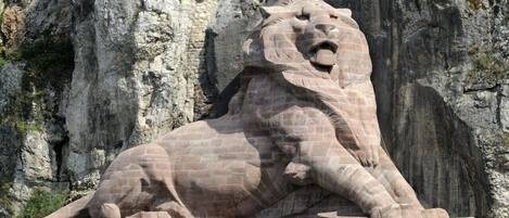 A stone lion statue with inscriptions, set against a rocky cliff backdrop.