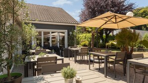 An outdoor patio with tables and chairs, a large umbrella, and potted plants.
