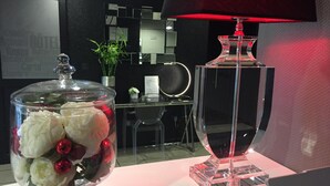 A glass display case with flowers and red ornaments, a clear glass bottle, and a red lamp on a table in a modern room with a black wall and a reception desk.