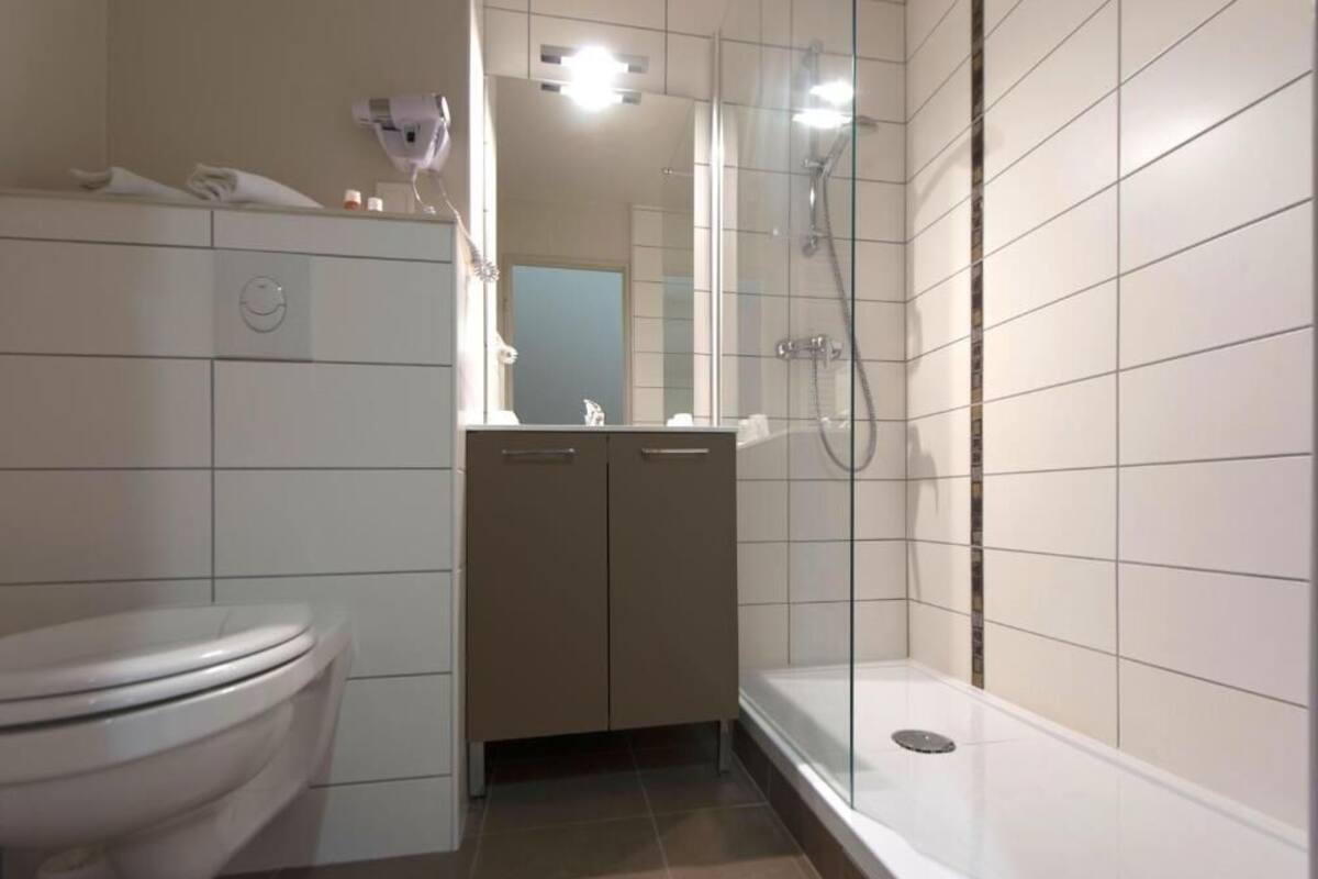 A bathroom with a toilet, a sink, a mirror, and a glass-enclosed shower area.