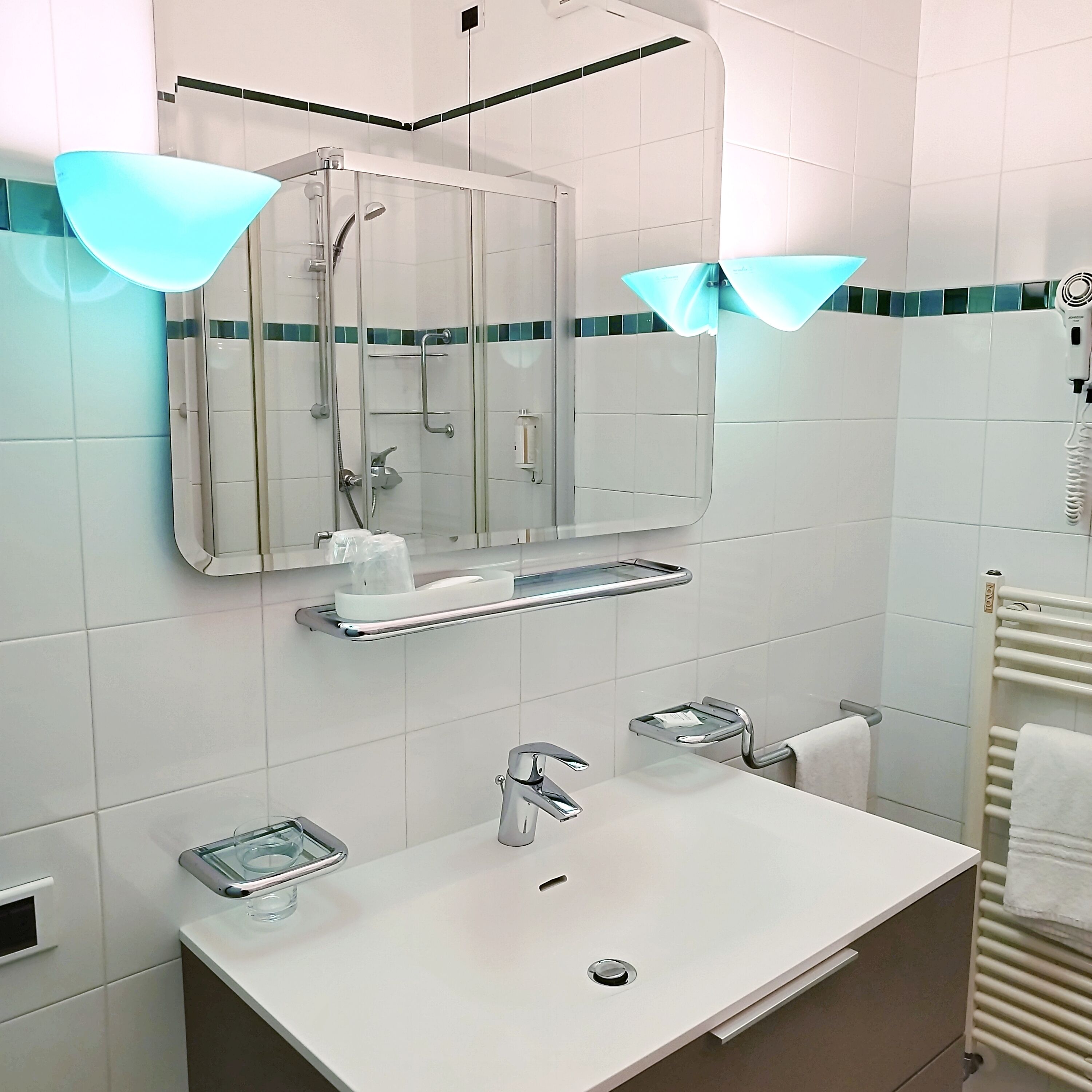 Un baño moderno con un espejo grande, un lavamanos, una ducha y un perchero para toallas.