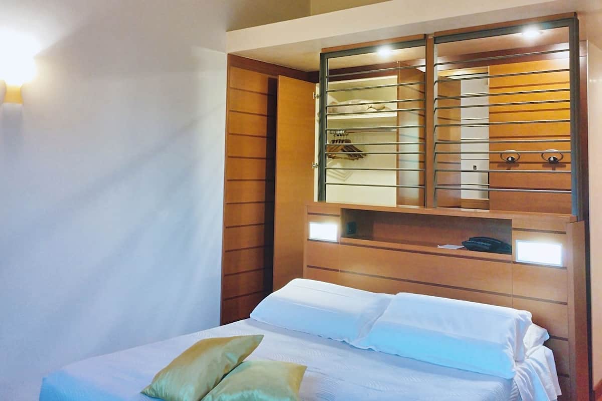 Une chambre à coucher comprenant un lit, une tête de lit en bois, un miroir et une armoire intégrée avec des étagères.
