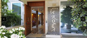 Entrada de un hotel con puerta de madera, mostrador de recepción y un letrero que dice "LAROCA".