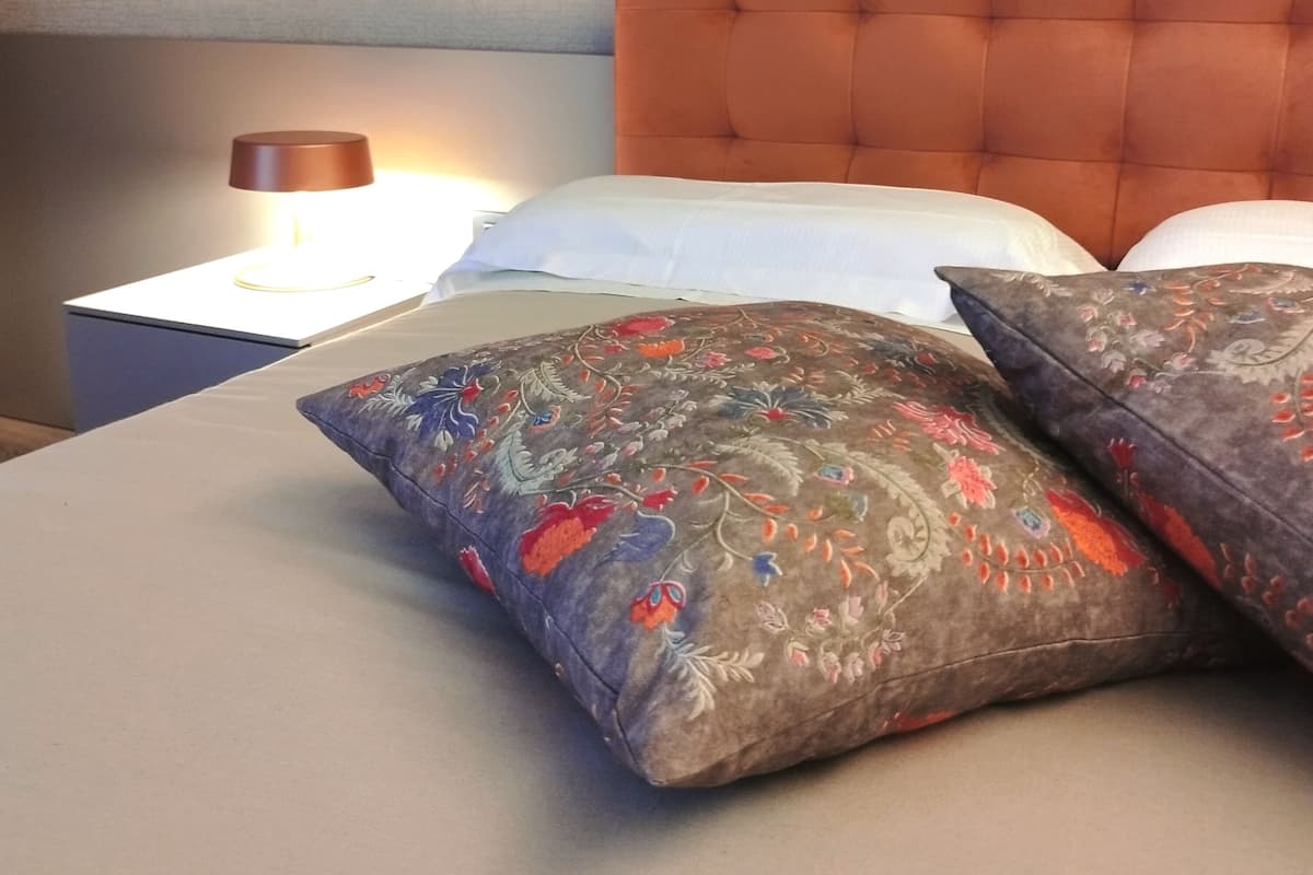 Un lit bien fait, avec une tête de lit capitonnée, une lampe de chevet et des coussins décoratifs.