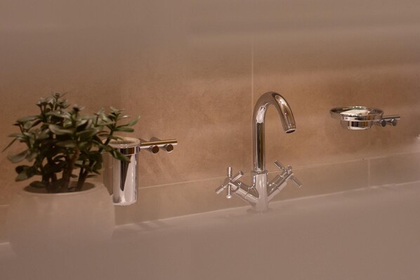 A bathroom with a modern chrome faucet, a small plant in a glass container, and a soap dish on the wall.