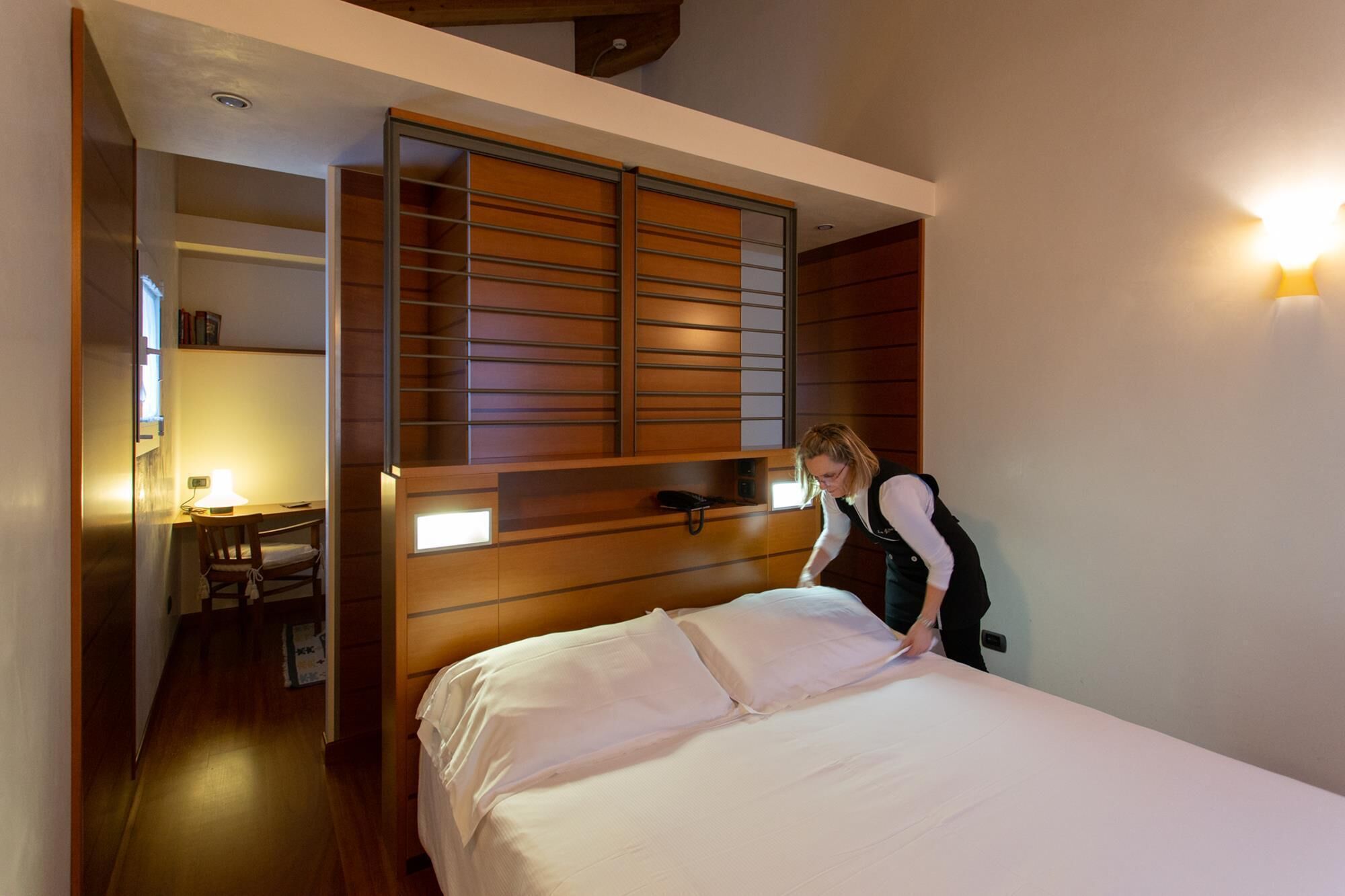 A bedroom with a bed, a desk, and a chair. There is a wooden wardrobe with a sliding door.