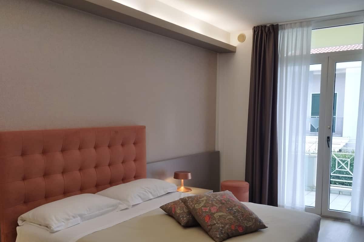 Une chambre d’hôtel avec un grand lit, une table de chevet, une lampe et une vue sur l’extérieur grâce à une porte vitrée.
